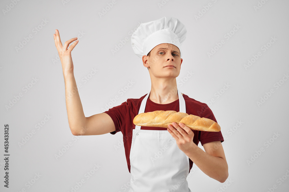 male baker in a white apron holding a loaf in hand cooking food male baker in a white apron holding a loaf in hand cooking food