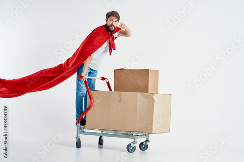 Cheerful man in a red cloak transport in a box light background