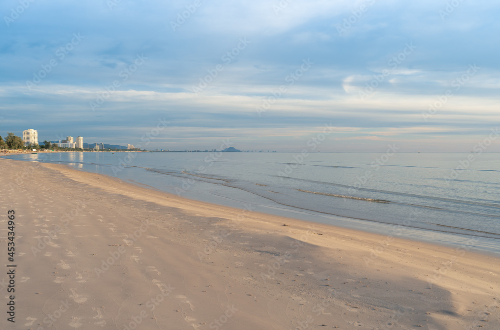 Early morning view of the serene Hua Hin Beach in Thailand, with its calm waters and soft sandy shore, under a pastel-colored sky.
