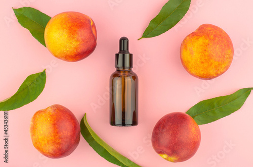 Natural peach oil. Natural cosmetics, hair care. Bottle with essential peach oil, peaches and green peach leaves on a pink background.