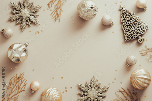 Elegant Christmas background. Frame border made of golden decorations, balls, confetti on beige table. Flat lay, top view, copy space. Xmas banner design, New Year greeting card mockup.