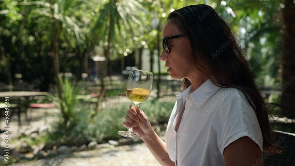 An adult woman a wine connoisseur is relaxing in a bar on the street with a glass of cold white wine during the day at the resort An adult woman a wine connoisseur is relaxing in a bar on the street with a glass of cold white wine during the day at the resort