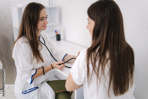 Female doctor using sphygmomanometer with stethoscope checking blood pressure to a patient in the hospital. Young woman modern in clinic