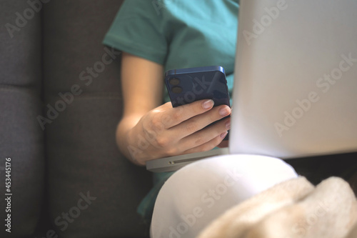 Woman in trendy clothes using mobile phone sitting on sofa at home in autumn weekends