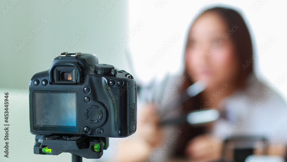Selective focus on camera, Young and beautiful Asian girl shows various face brushes to camera with smile and happy during broadcast video recording about cosmetics content and review.