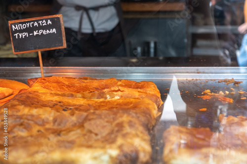 Fototapeta Naklejka Na Ścianę i Meble -  Bougatsa, traditional pastry with cream or cheese in a shop display, street food. Label with text in Greek