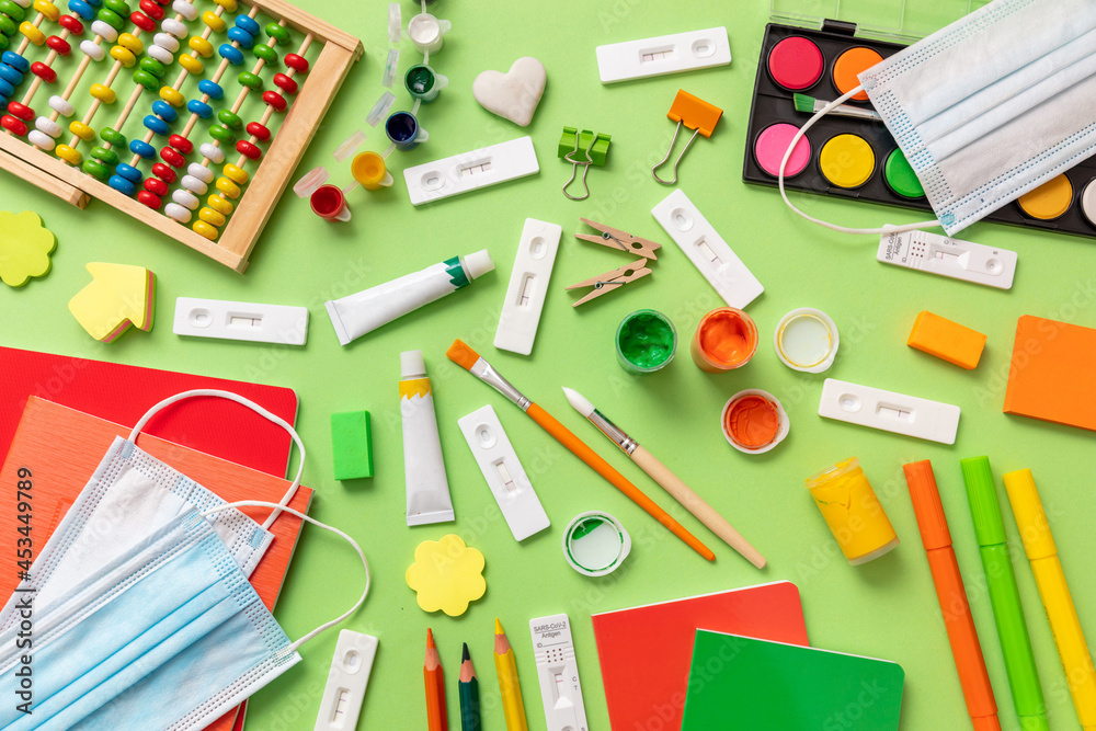 Back to school Covid 19 days. School supplies and Coronavirus measures flat lay. Rapid test, protective medical mask and stationery on green background Back to school Covid 19 days. School supplies and Coronavirus measures flat lay. Rapid test, protective medical mask and stationery on green background