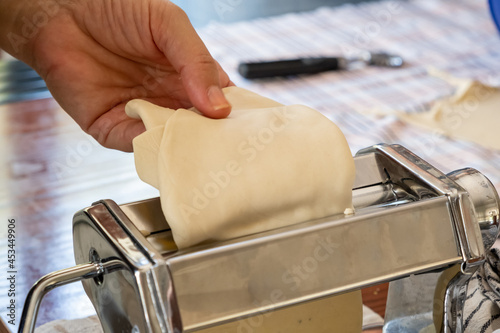 Pasta maker machine, Fresh pasta homemade preparation. Hand putting dough on the maker closeup view © Rawf8