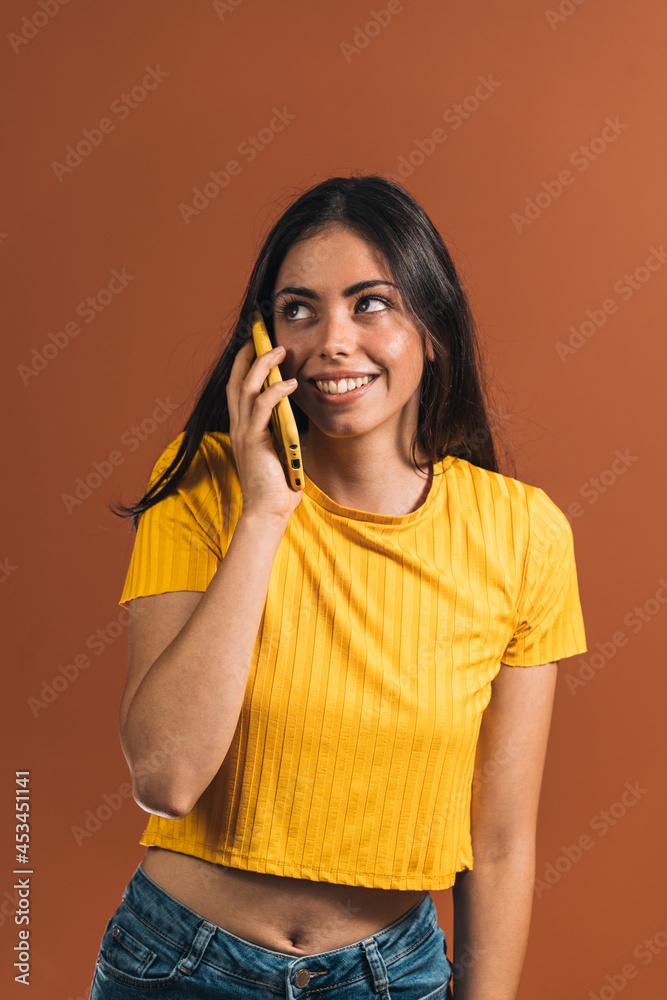 Vertical shot of smiling Caucasian female model in a yellow t-shirt posing with a smartphone Vertical shot of smiling Caucasian female model in a yellow t-shirt posing with a smartphone