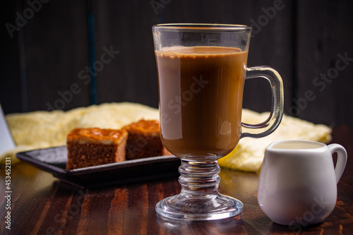Hot espresso coffee in a clear glass and cakes on wooden background