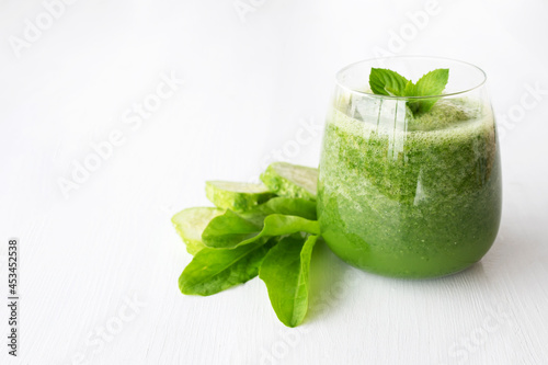 Raw green smoothie with herbs and cucumber on white wooden background.