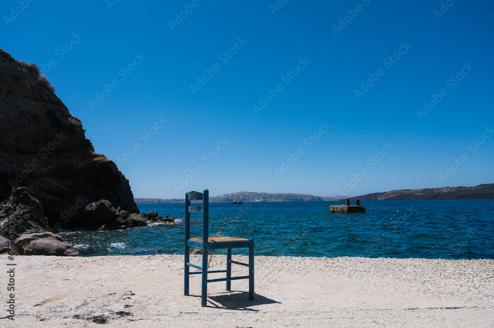 Old port of Thira on Santorini island. Old blue wooden chair near sea. Rocks and sea. Caldera view.