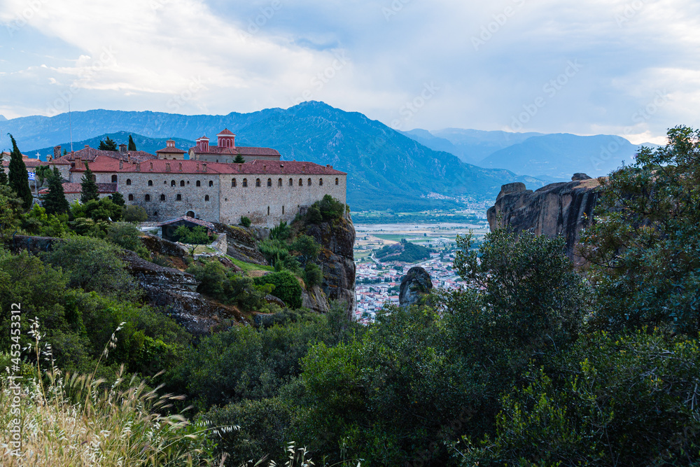 ギリシャ　メテオラの断崖絶壁の岩山の上に建つ聖ステファノス修道院と奇岩群の隙間から覗くカランバカの街並みと後ろに広がるピンドス山脈