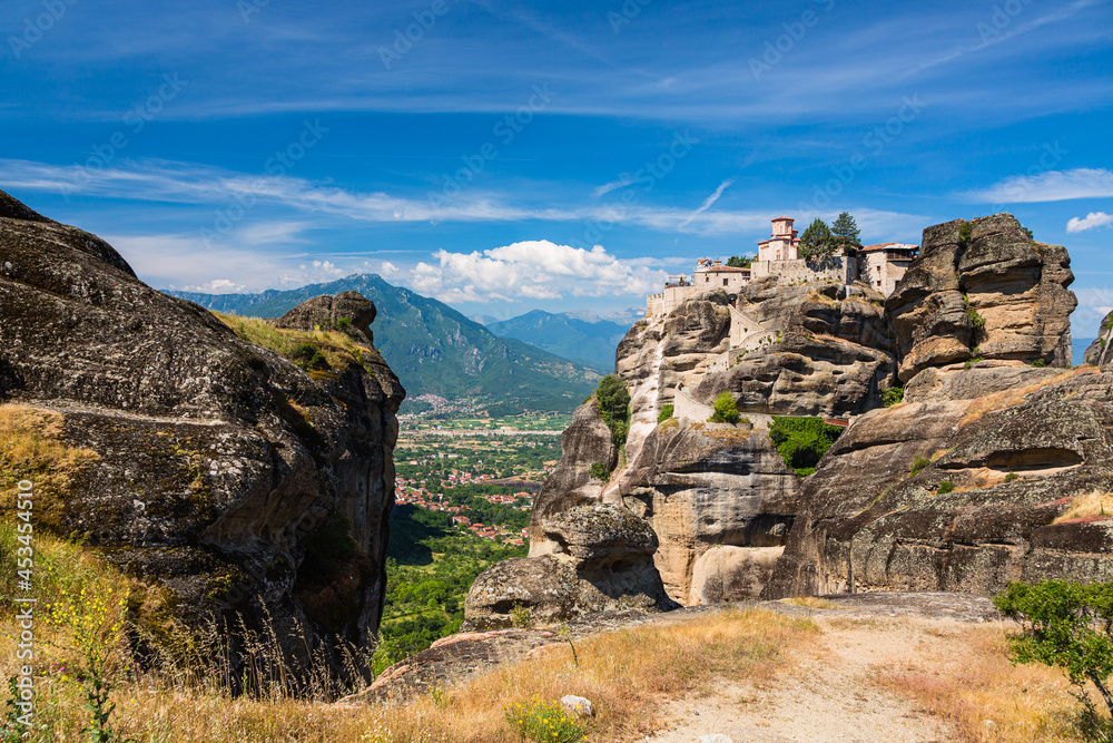 ギリシャ　メテオラの断崖絶壁の岩山の上に建つヴァルラアム修道院と奇岩群の隙間から見えるカランバカの街並みと後ろに見えるピンドス山脈