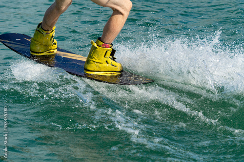 Wakeboard on a wave in motion. Blurry legs of a wakeboarder in boots. Splashes are flying from under the board.