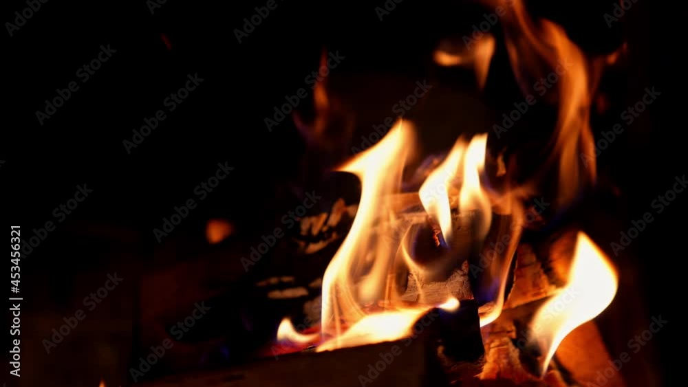 Orange flame in fireplace on black background. Wooden logs in fire flame. Warm cosy fire burning in fireplace. Close-up.