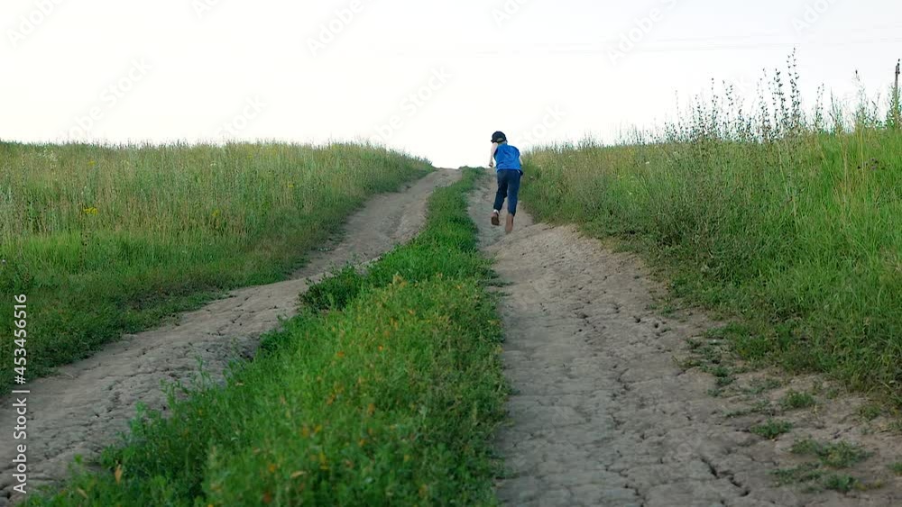 Carefree childhood theme. A child 6-8 years old runs along the road in the countryside on a summer day. The boy goes up the slope of the road. Rest and positive emotions in nature Carefree childhood theme. A child 6-8 years old runs along the road in the countryside on a summer day. The boy goes up the slope of the road. Rest and positive emotions in nature