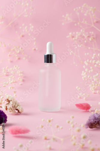 Cosmetic bottle with flowers on pink background. Close up