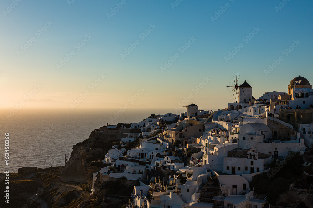 ギリシャ　サントリーニ島のイアのイア・キャッスルから見えるマジックアワーの海に沈み行く夕日と白い街並みと風車