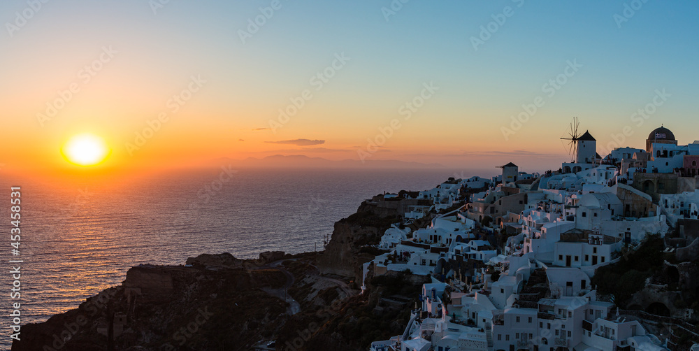 ギリシャ　サントリーニ島のイアのイア・キャッスルから見えるマジックアワーの海に沈み行く夕日と白い街並みと風車
