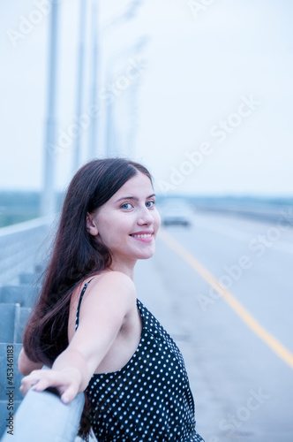 Portrait of a happy girl with long hair in a black dress near an empty road