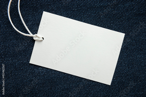 Cardboard tag on jeans texture with place for text. Empty label blank on cloth. Sale, discount and shopping concept