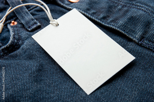 Cardboard tag on jeans texture with place for text. Empty label blank on cloth. Sale, discount and shopping concept