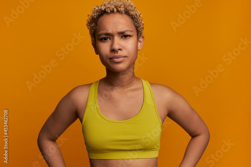 Anger. Image of frowning angry youthful African American woman in yellow top with nose ring, looking at camera with discontent face expression, feeling displeased and upset with bad behavior