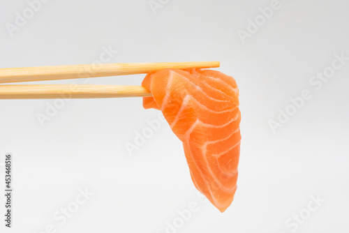 Sashimi-style salmon with chopsticks on a white background, ready to eat.