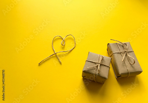 Gift wrapping in kraft paper with a heart made of threads on a yellow background. Minimalism. The concept of the holiday, love, birthday. Place for text, romantic wallpaper. Flat lay, top view
