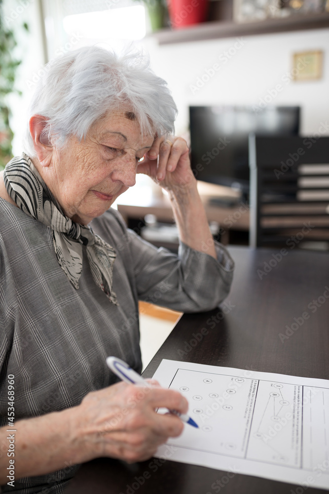 Focused senior gray-haired Caucasian woman doing Self-Administered Gerocognitive Examination test in her home. Loneliness and aging concept