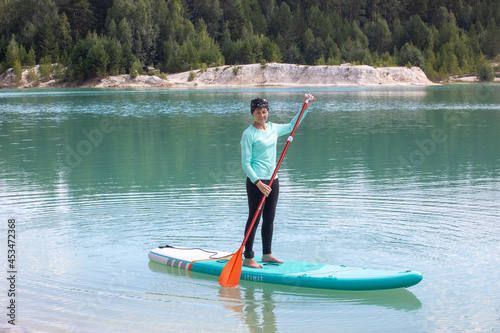 A girl in a dress floats on a glanders board on a pond with bright turquoise water. Warm summer day for travel.  photo