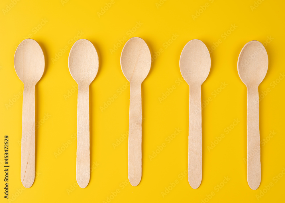 High angle view of bamboo spoons arranged in a row on a yellow background