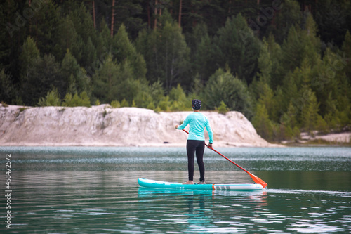 A girl in a dress floats on a glanders board on a pond with bright turquoise water. Warm summer day for travel.  photo