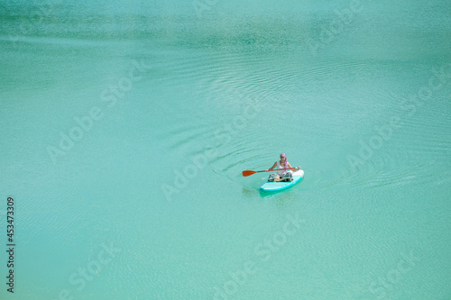 A girl in a dress floats on a glanders board on a pond with bright turquoise water. Warm summer day for travel.  © Sergei Malkov