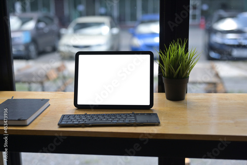 Blank screen tablet with keyboard on wooden working desk.