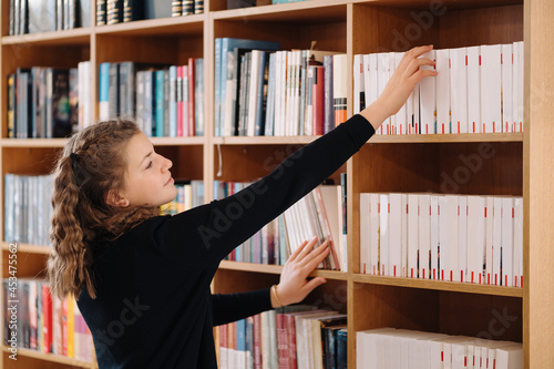 Happy tenage girl or student taking book from shelf in library - People, knowledge, education and school concept photo