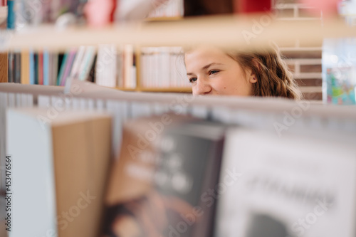 Happy tenage girl or student taking book from shelf in library - People, knowledge, education and school concept photo