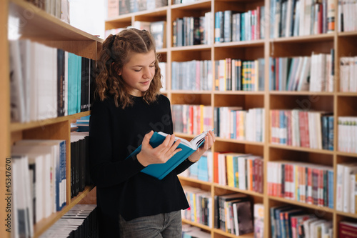 Teen girl among a pile of books. A young girl reads a book with shelves in the background. She is surrounded by stacks of books. Book day.