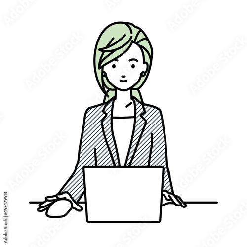 デスクで座ってPCを使っているスーツの女性