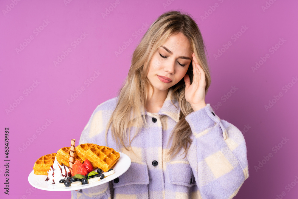 Teenager Russian girl holding waffles isolated on purple background with headache Teenager Russian girl holding waffles isolated on purple background with headache