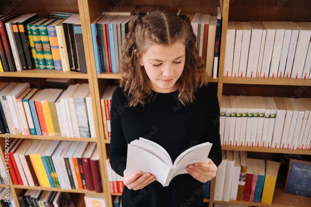 Teen girl among a pile of books. A young girl reads a book with shelves in the background. She is surrounded by stacks of books. Book day. Teen girl among a pile of books. A young girl reads a book with shelves in the background. She is surrounded by stacks of books. Book day.