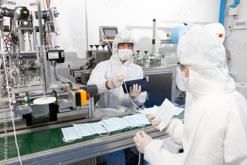 male engineers wearing personal protective equipment uniform PPE   producing medical face mask beside machine in laboratory