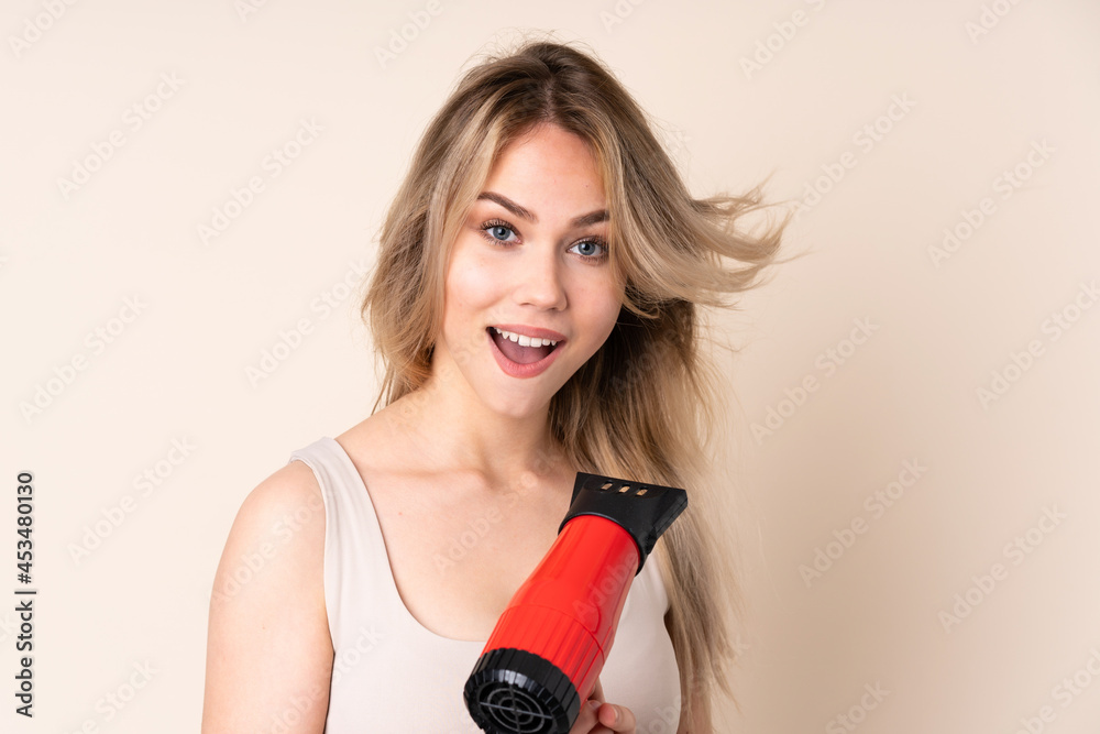 Teenager blonde girl with hairdryer over isolated background Teenager blonde girl with hairdryer over isolated background