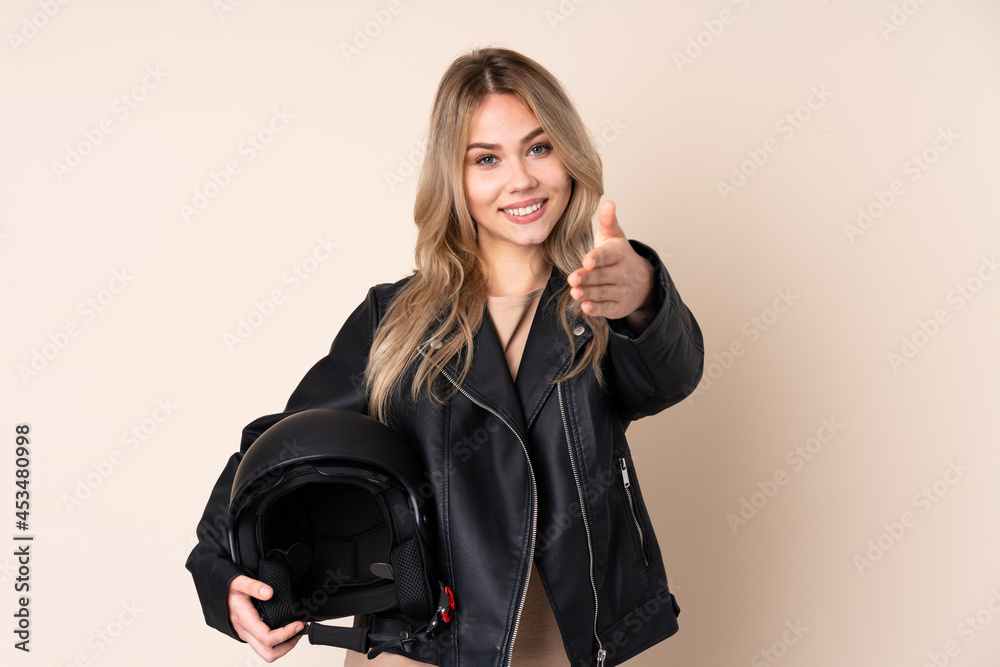 Russian girl with a motorcycle helmet isolated on beige background shaking hands for closing a good deal Russian girl with a motorcycle helmet isolated on beige background shaking hands for closing a good deal