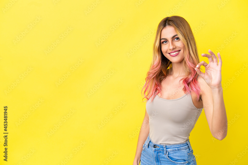 Young woman over isolated yellow background showing ok sign with fingers Young woman over isolated yellow background showing ok sign with fingers