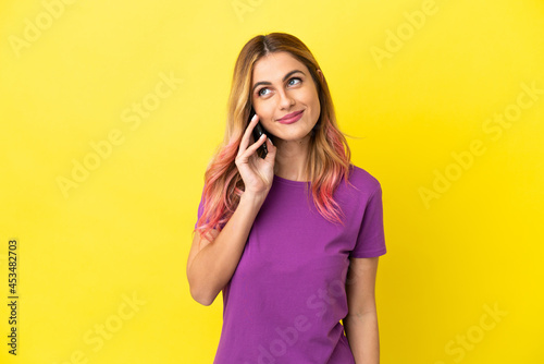 Young woman using mobile phone over isolated yellow background thinking an idea while looking up © luismolinero