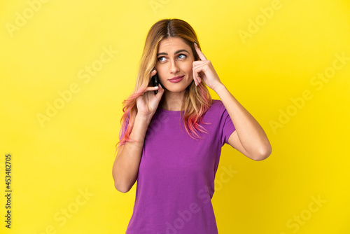 Young woman using mobile phone over isolated yellow background having doubts and thinking