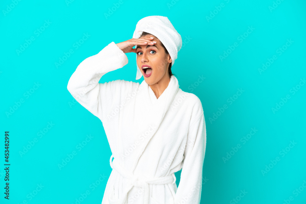 Young woman in a bathrobe over isolated blue background doing surprise gesture while looking to the side Young woman in a bathrobe over isolated blue background doing surprise gesture while looking to the side