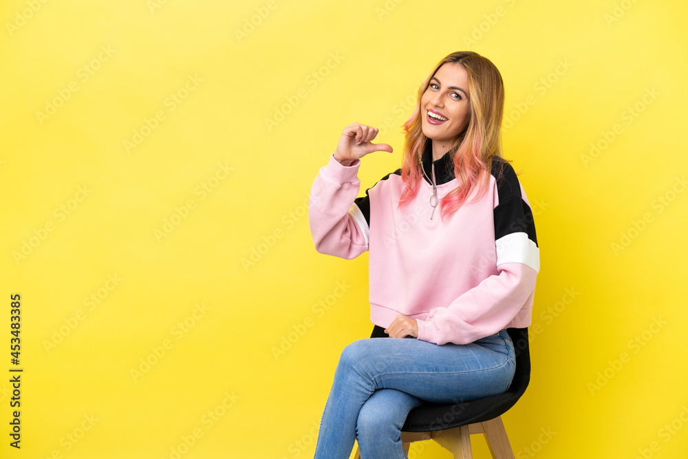 Young woman sitting on a chair over isolated yellow background proud and self-satisfied